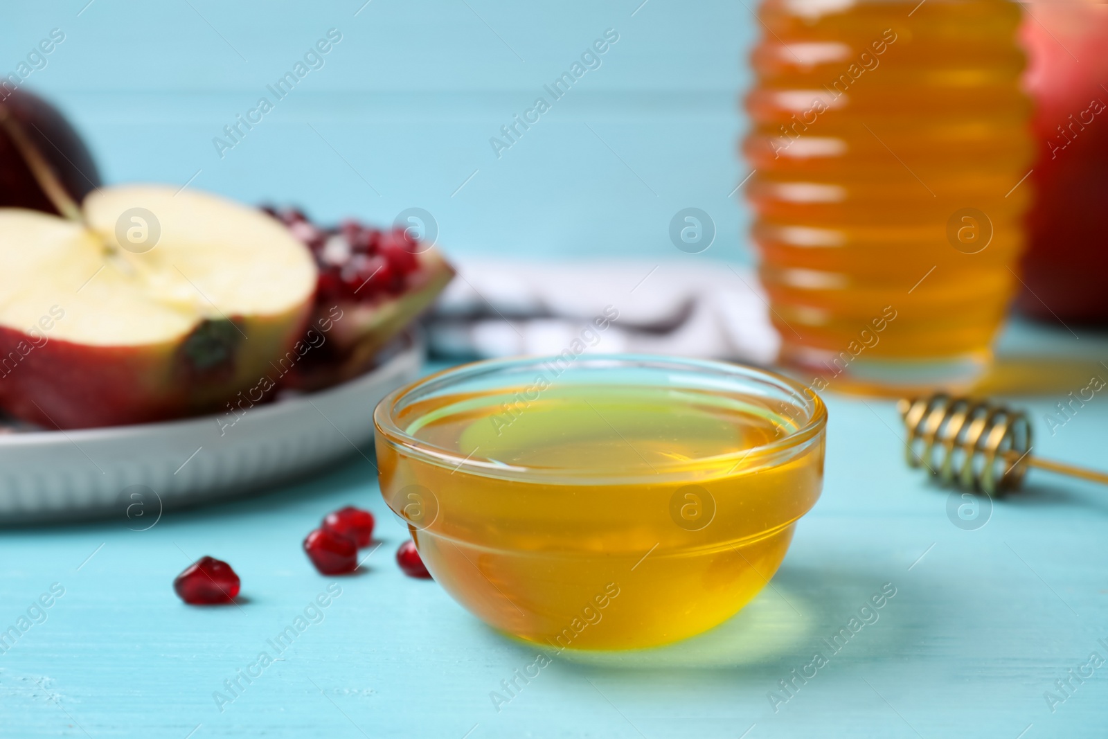 Photo of Honey, pomegranate seeds and apples on light blue wooden table. Rosh Hashanah holiday