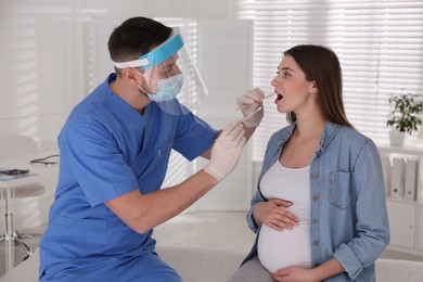 Photo of Doctor taking throat smear of pregnant woman for coronavirus test in clinic