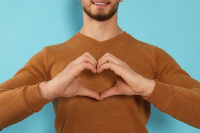 Photo of Happy volunteer making heart with his hands on light blue background, closeup