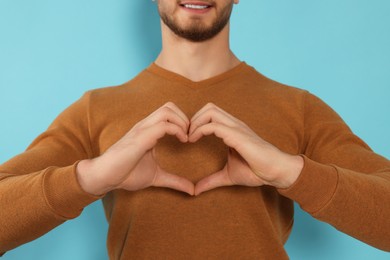 Happy volunteer making heart with his hands on light blue background, closeup