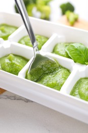 Photo of Putting puree with spoon into ice cube tray on table, closeup. Ready for freezing