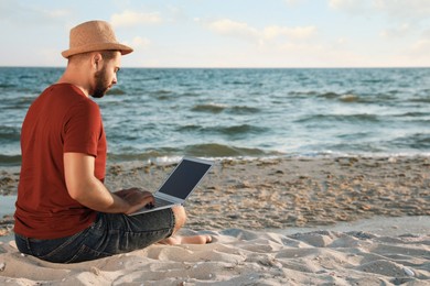 Photo of Man working with laptop on beach. Space for text