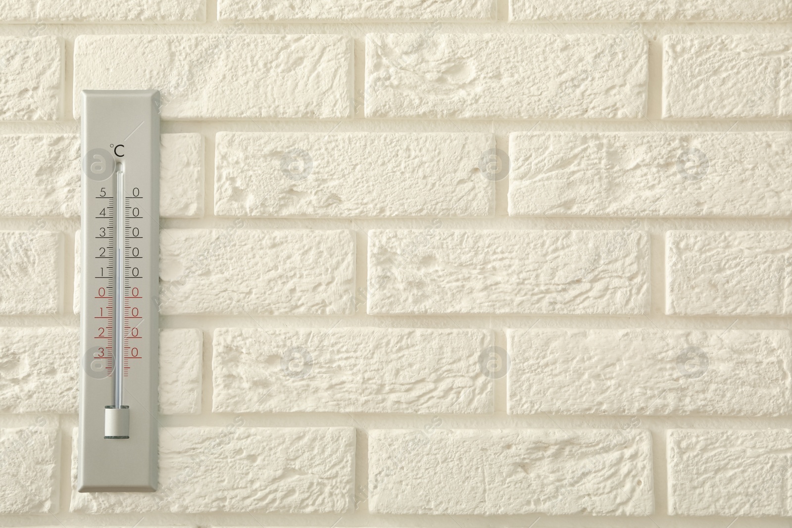 Photo of Weather thermometer on white brick wall. Space for text