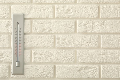 Photo of Weather thermometer on white brick wall. Space for text