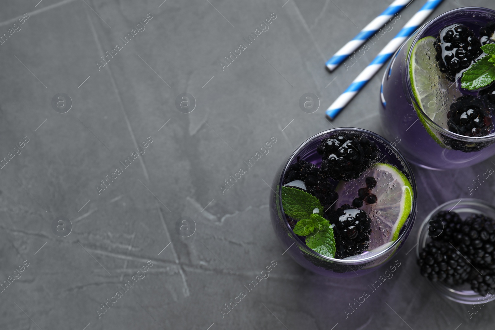 Photo of Delicious blackberry lemonade made with soda water  on grey table, flat lay. Space for text