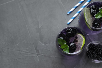 Photo of Delicious blackberry lemonade made with soda water  on grey table, flat lay. Space for text