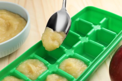 Photo of Putting apple puree ice cube tray on wooden table, closeup. Ready for freezing