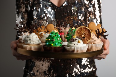 Photo of Woman holding tasty Christmas cupcakes on light background, closeup