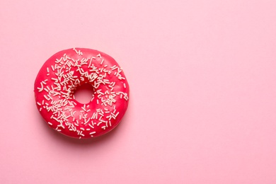 Delicious glazed doughnut with sprinkles on color background, top view