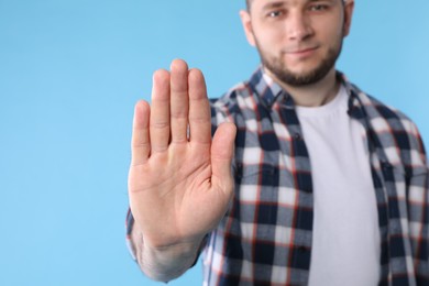 Man showing gesture stop on light blue background, closeup