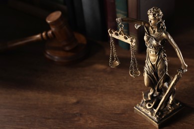 Photo of Statue of Lady Justice near books and gavel on wooden table, space for text. Symbol of fair treatment under law
