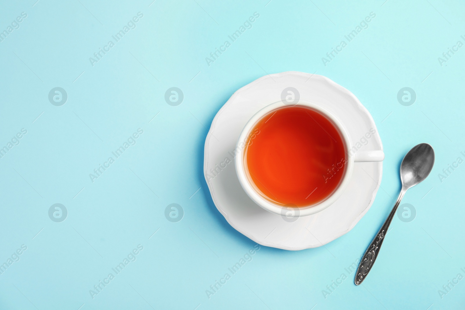 Photo of Cup of delicious tea with saucer and spoon on color background, top view