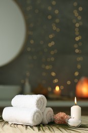 Photo of Spa composition. Rolled towels, sea salt and burning candles on table against blurred lights, space for text