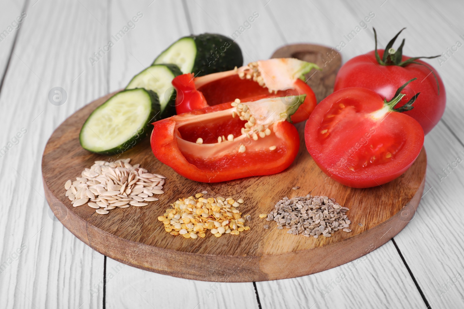 Photo of Fresh cucumbers, red bell peppers, tomatoes and vegetable seeds on white wooden table, closeup