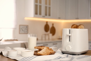 Modern toaster and tasty breakfast on wooden table in kitchen