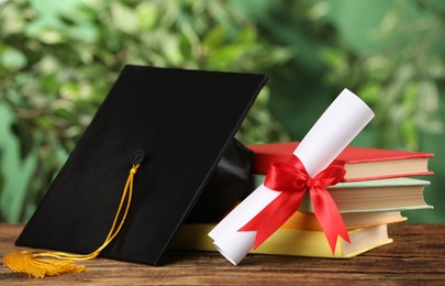 Photo of Graduation hat, books and diploma on wooden table against blurred background