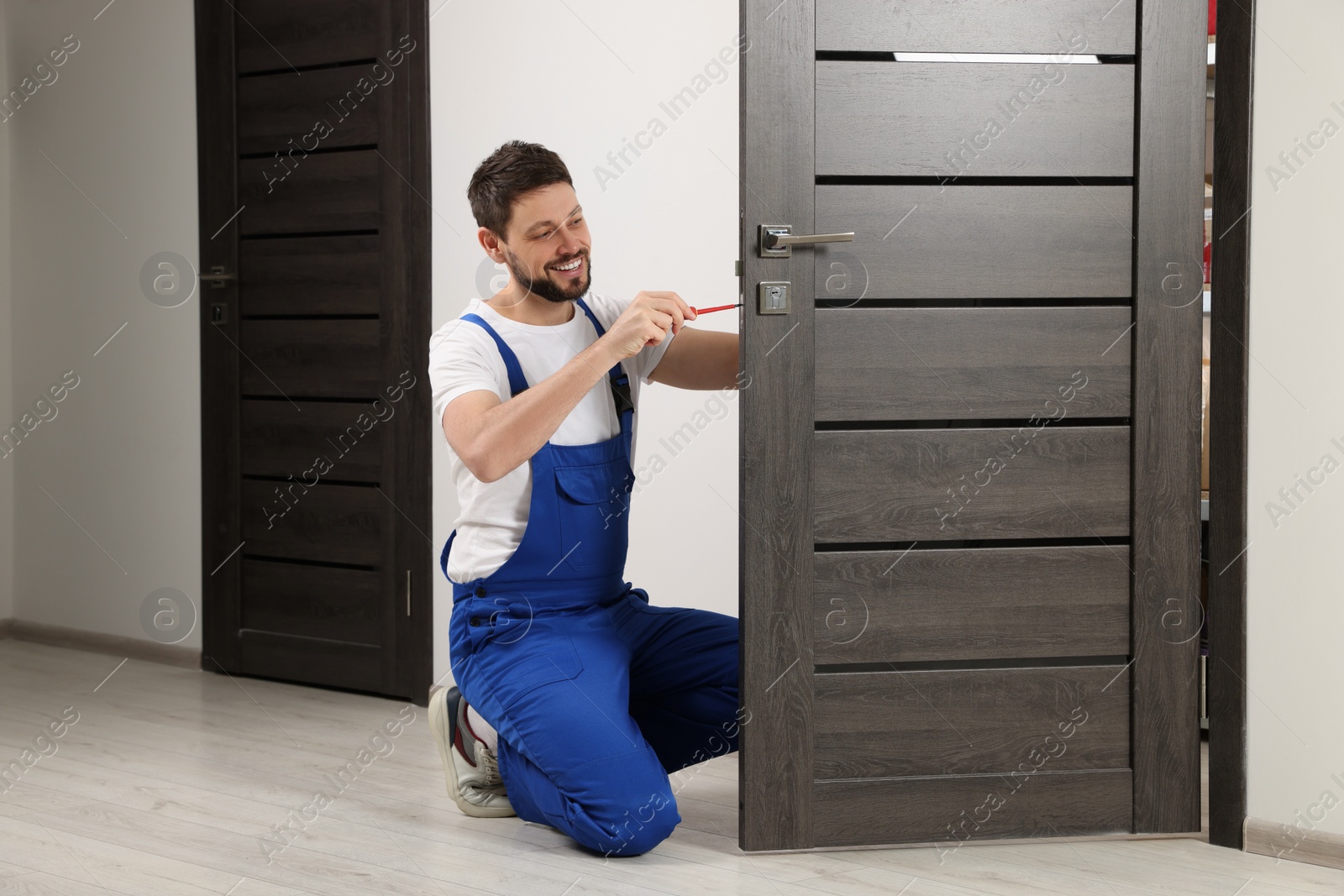 Photo of Worker in uniform with screwdriver repairing door lock indoors