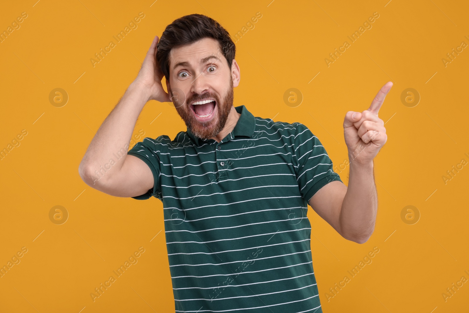 Photo of Surprised man pointing at something on yellow background