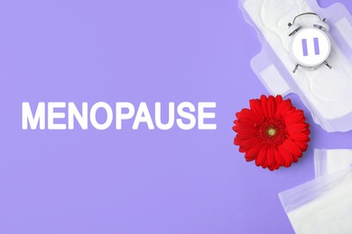 Menopause word, alarm clock with pause symbol, flower and pads on violet background, flat lay