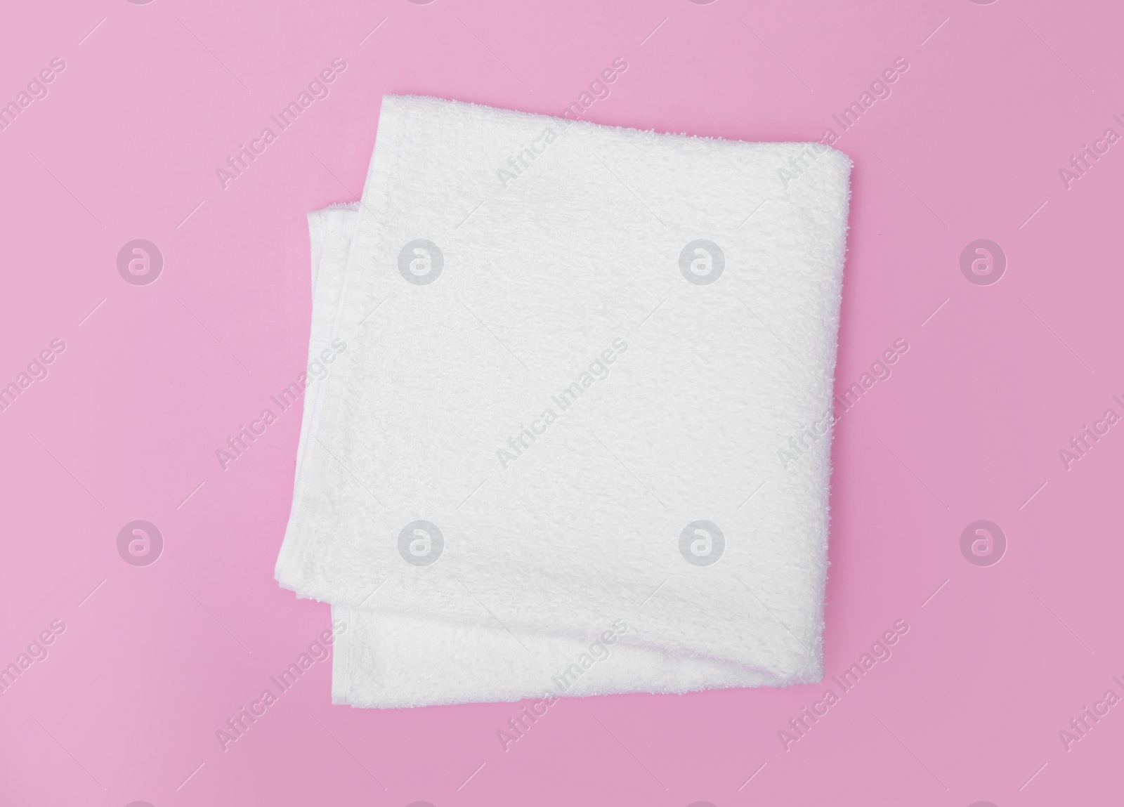 Photo of Folded white beach towel on pink background, top view