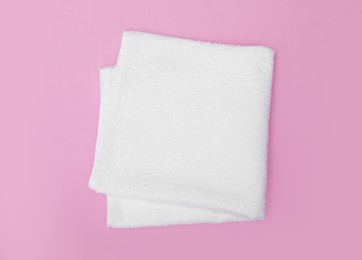 Folded white beach towel on pink background, top view