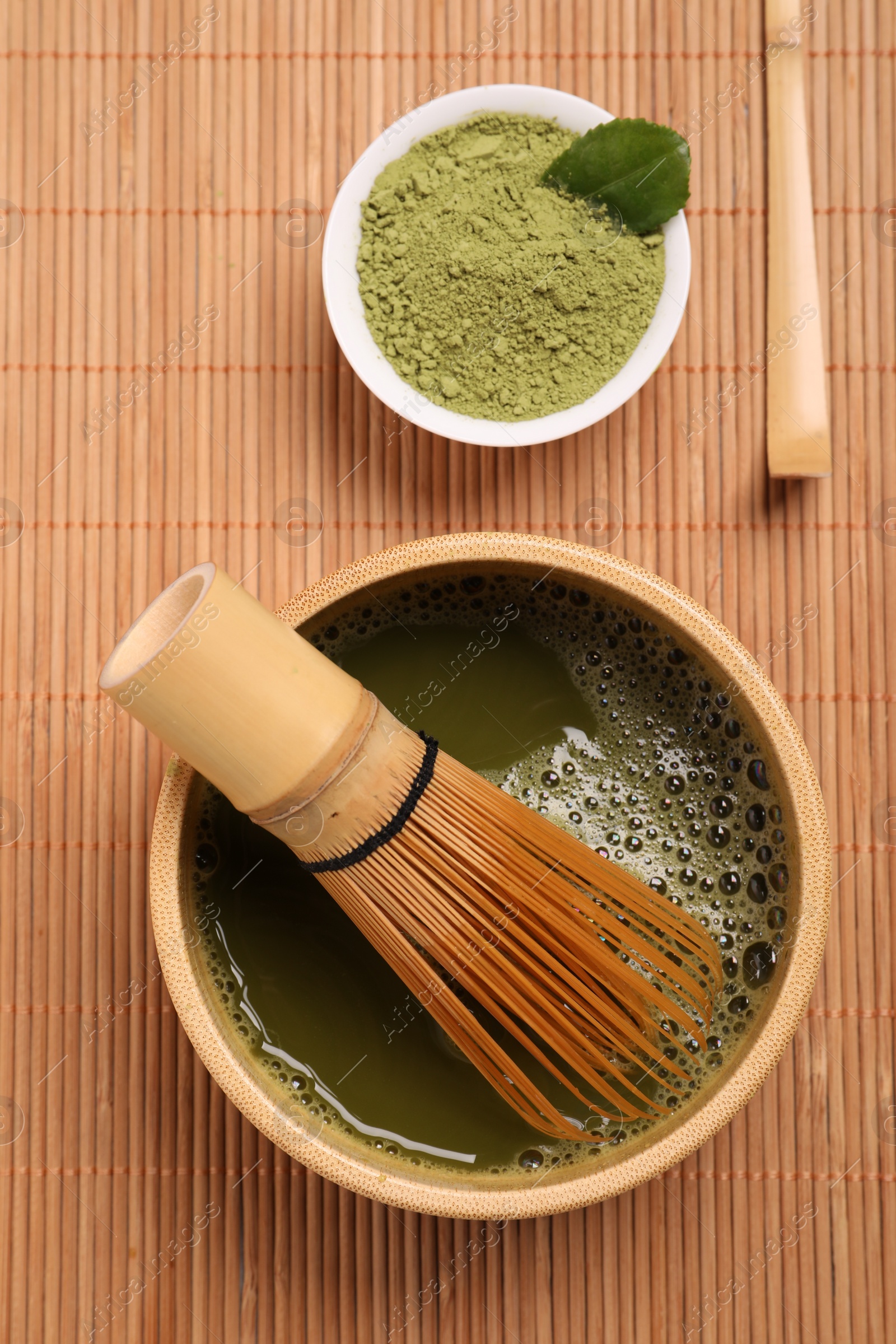 Photo of Bowl of fresh matcha tea with whisk and powder on bamboo mat, flat lay