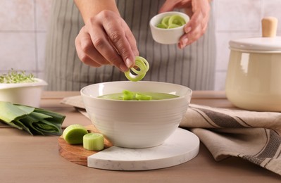 Photo of Woman putting cut leek into bowl of tasty soup at wooden table, closeup