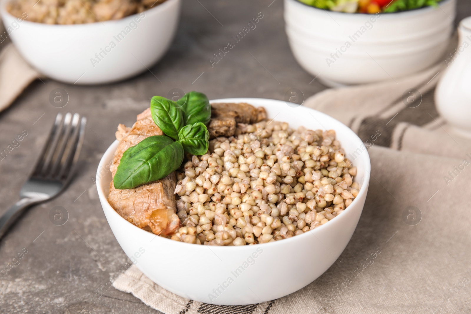 Photo of Tasty buckwheat porridge with meat on grey table