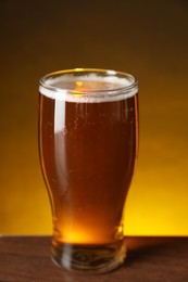 Photo of Glass with fresh beer on wooden table against dark background, closeup