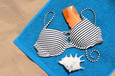 Photo of Blue beach towel, seashell, sunscreen and swimsuit on sand, top view