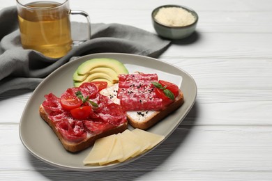 Photo of Tasty toasts with slices of sausages, tomatoes and cheese on white wooden table