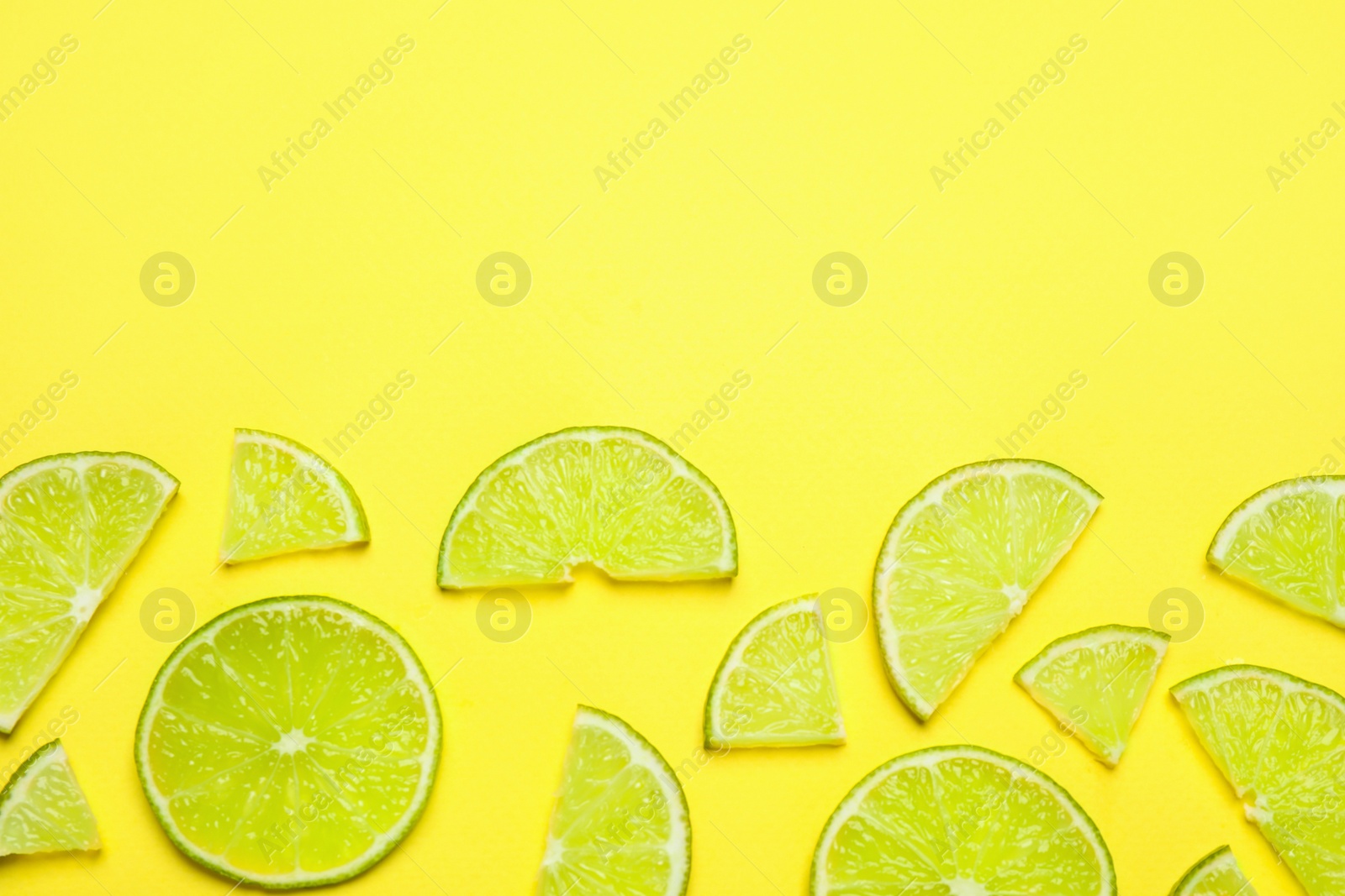 Photo of Juicy fresh lime slices on yellow background, flat lay. Space for text