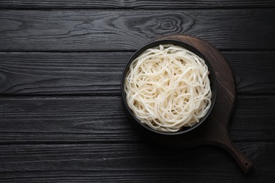 Photo of Bowl of tasty cooked rice noodles on black wooden table, top view. Space for text