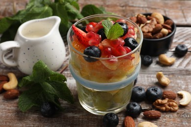 Delicious fruit salad, fresh berries, mint and nuts on wooden table