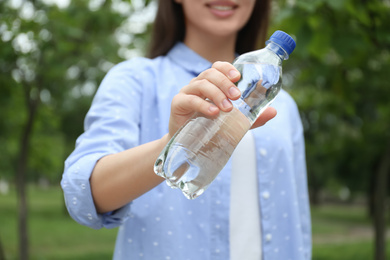 Photo of Woman holding bottle with water outdoors, closeup