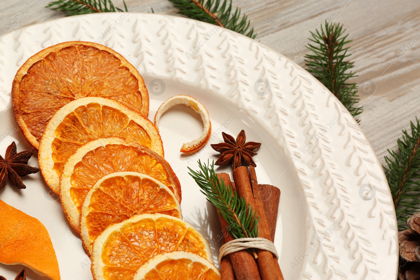 Photo of Plate with dry orange slices, anise stars and cinnamon sticks on white wooden table, closeup