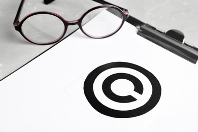 Photo of Clipboard with copyright symbol and glasses on table, closeup. Law compliance concept