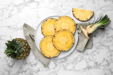 Slices of tasty ripe pineapple and whole fruit on white marble table, flat lay