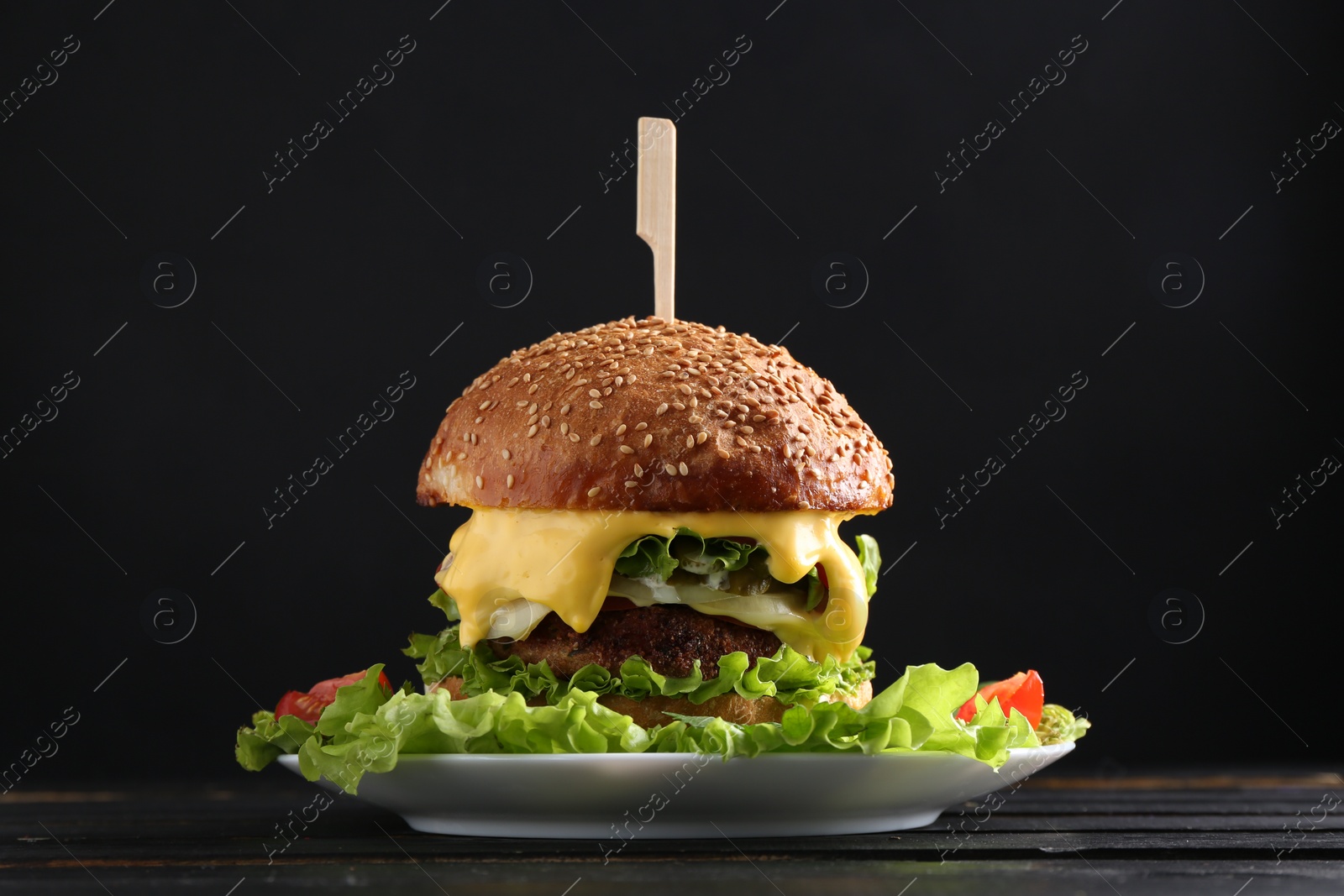 Photo of Vegetarian burger with delicious patty and cheese on black wooden table