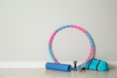 Hula hoop, yoga mat, bag and dumbbells near light wall in gym. Space for text