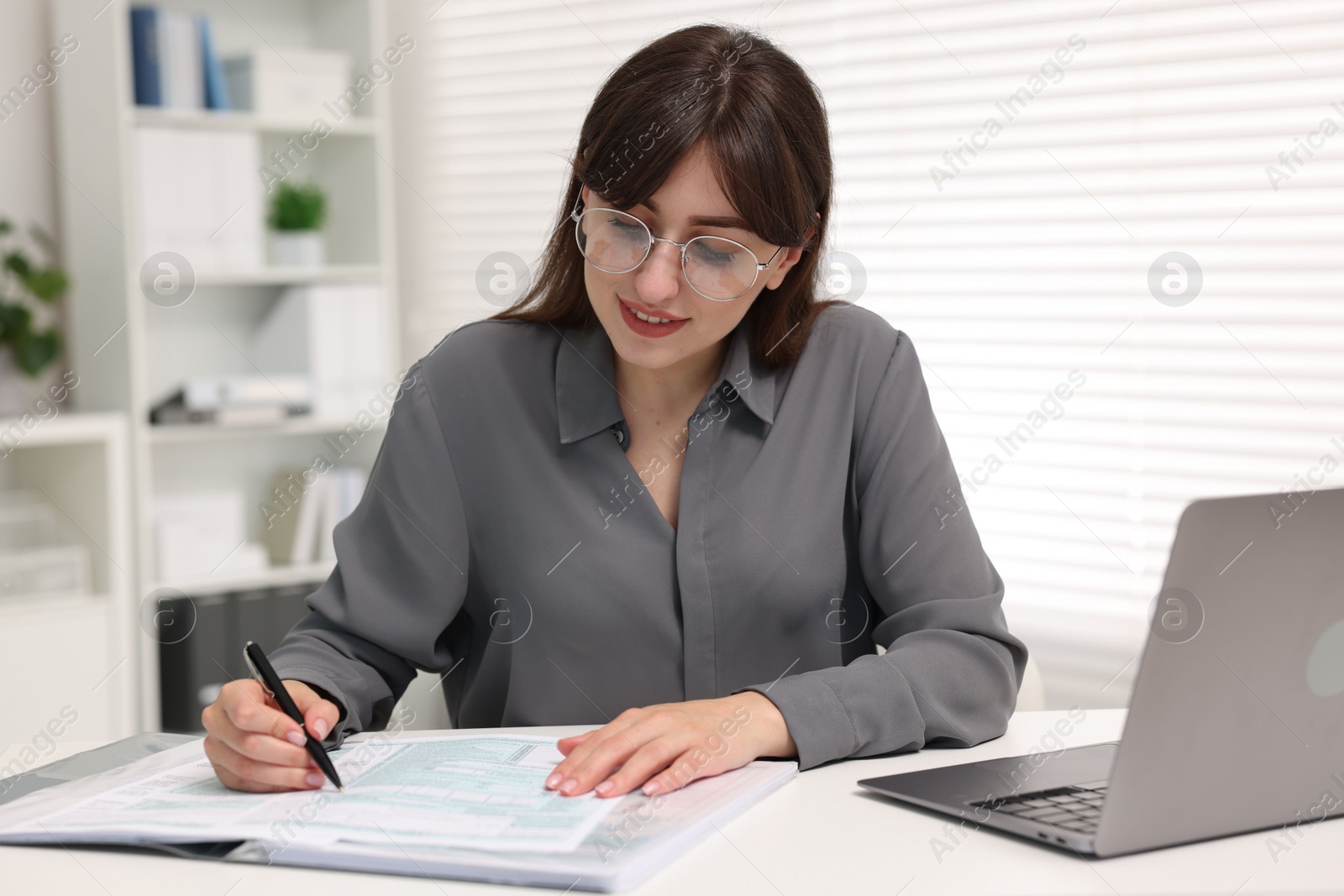 Photo of Smiling secretary doing paperwork at table in office