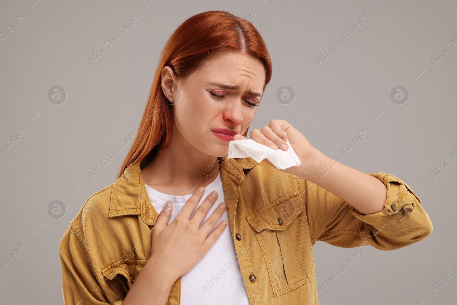 Photo of Suffering from allergy. Young woman with tissue sneezing on grey background