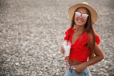 Photo of Beautiful young woman with tasty milk shake on beach, space for text