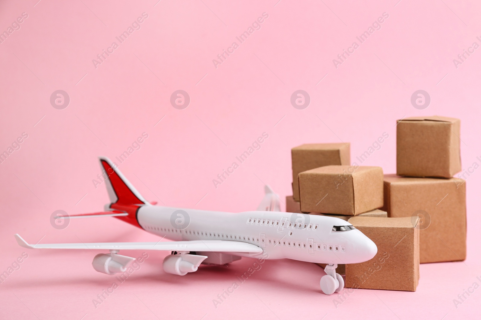 Photo of Airplane model and carton boxes on light pink background. Courier service