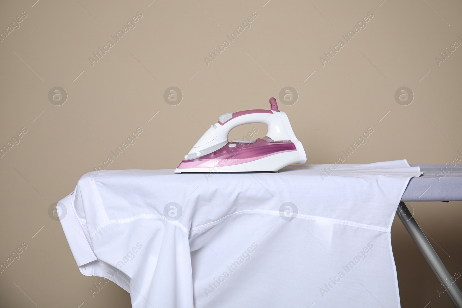 Photo of Modern iron and clean shirt on board against beige background