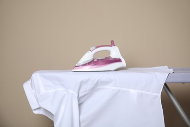 Photo of Modern iron and clean shirt on board against beige background