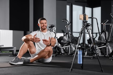 Trainer streaming online workout with phone at gym
