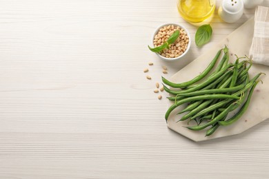 Board with fresh green beans and different ingredients on white wooden table, flat lay. Space for text