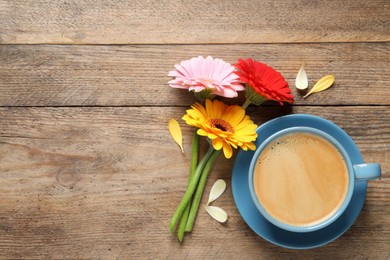 Beautiful colorful gerbera flowers, petals and cup of coffee on wooden table, flat lay. Space for text
