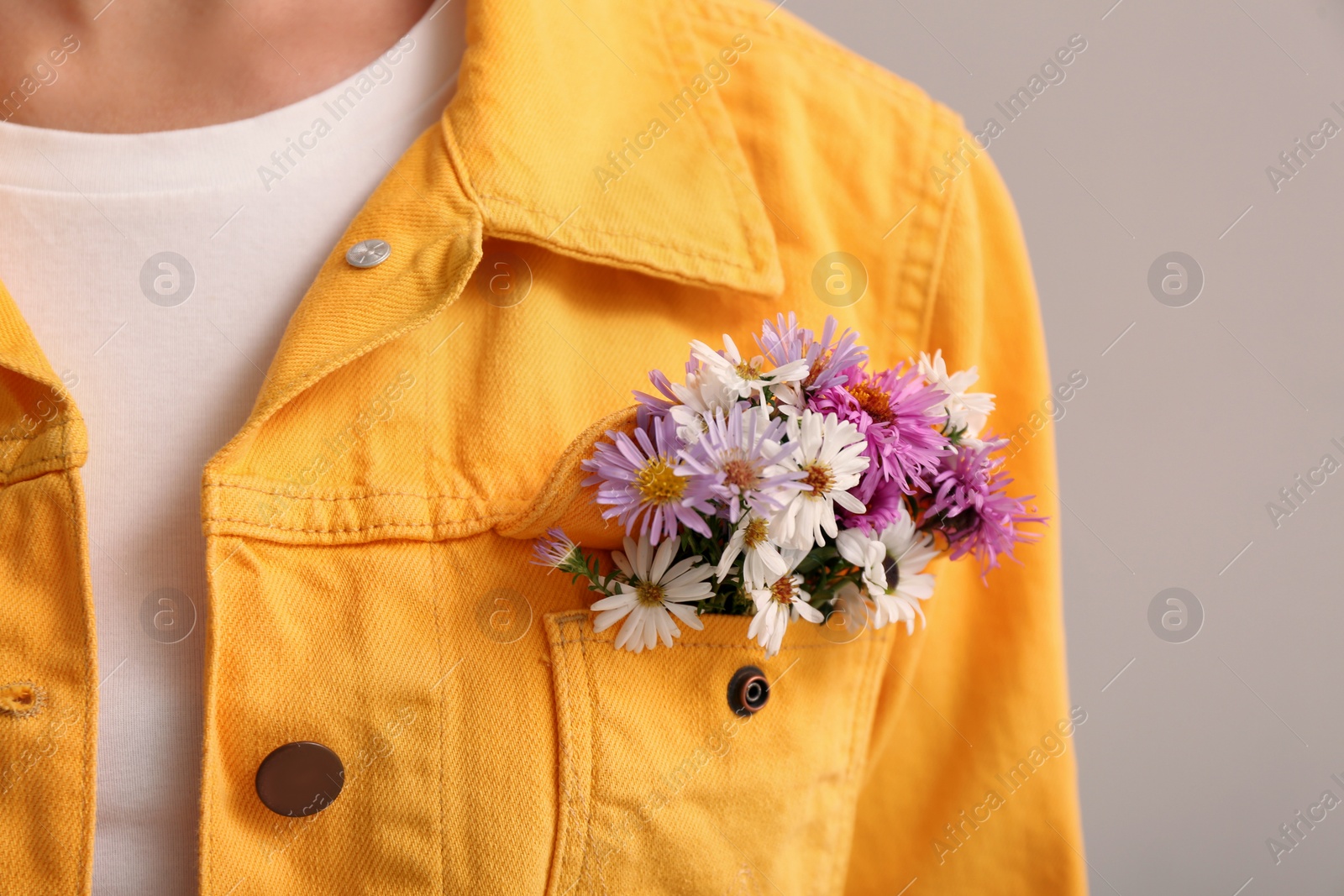 Photo of Woman with beautiful tender flowers in jacket's pocket on light background, closeup